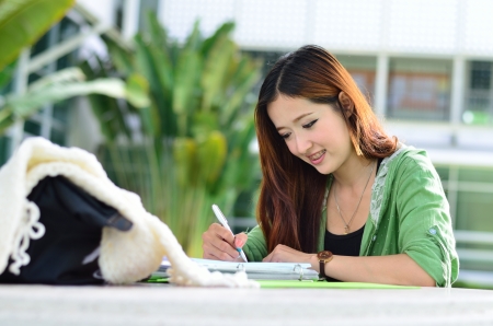 Beautiful young asian student is reading and writing homeworkの写真素材