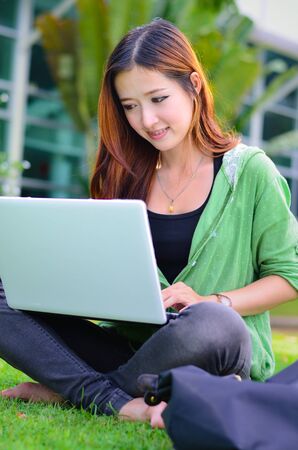 Beautiful young asian student smiling with computer notebook at gardenの写真素材