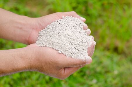 Farmer hand holding plant chemical fertilizer over green backgroundの写真素材