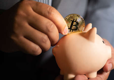 Hand saving bitcoins cryptocurrency in to a piggy bankの写真素材