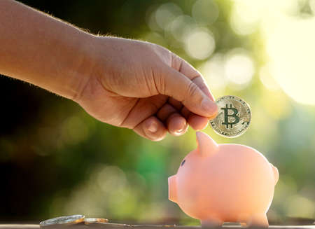 Hand saving bitcoins cryptocurrency in to a piggy bankの写真素材