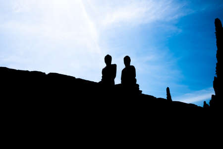 Silhouette of two Buddha statues with blue sky as background