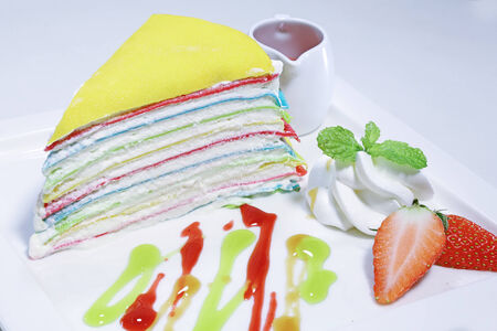 A rainbow cake decorated with a berries on the top and cup of tea. Isolated on white background. の写真素材