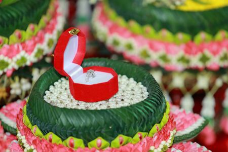 A diamond wedding ring in an open box on traditional Thai style garlandの写真素材