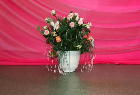 Bouquet of artificial flowers in white pot at background of pink drapesの写真素材