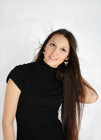beautiful brunette girl wearing black dress looks up and smiles in white studioの写真素材