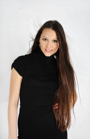 beautiful brunette girl wearing black dress looks at camera and smiles in white studioの写真素材