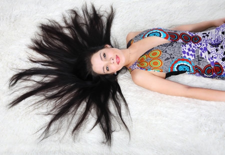 Beautiful girl wearing dress lies on white fur inside studioの写真素材