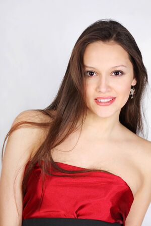 Beautiful brunette girl wearing red dress smiles in white studioの写真素材