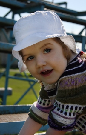 Cute little girl wearing white panama climbs on playground and looks at cameraの写真素材