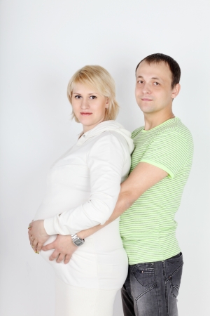 Happy pregnant wife in white and husband hold belly on white background の写真素材