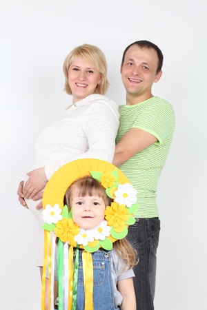Happy pregnant wife and husband hold belly and little daughter stands near them on white background  Focus on parents の写真素材