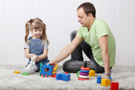 Happy little daughter and her father play toys on soft carpet at home の写真素材