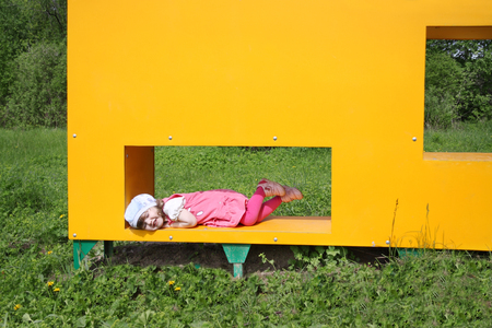Happy little cute girl lies in window of yellow box at playground at summer day outdoors. の写真素材