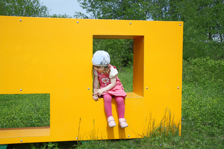 Happy little cute girl sits in window of yellow box at playground at summer day. の写真素材