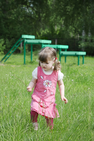 Little girl runs in grass near playground at summer day outdoors. の写真素材