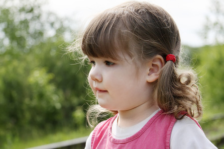 Little cute girl in pink dress thinks and looks away at summer day.  の写真素材