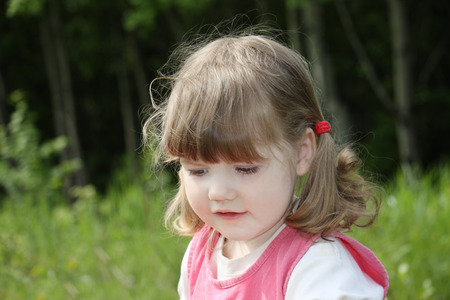 Little beautiful girl in pink dress looks down at summer day.  の写真素材