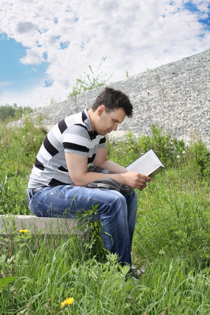 Young man in jeans intently reads book outdoor at summer day.  の写真素材