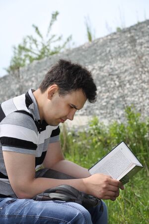 Young brunet man in jeans intently reads book outdoor at summer day.  の写真素材