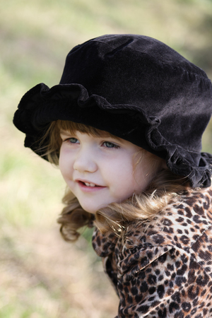 Beautiful little girl in black hat looks away outdoor at autumn day.の写真素材