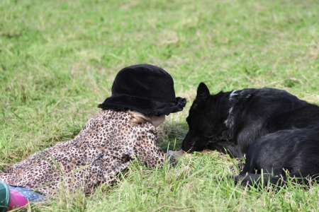 Little girl in black hat lies on grass with black dog at autumn day.の写真素材