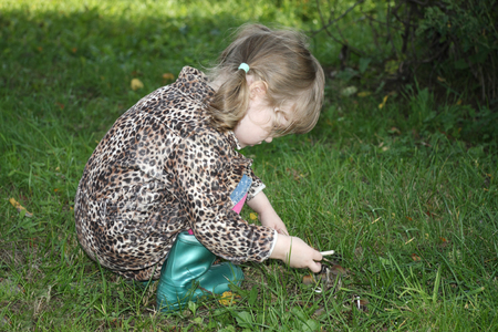 Cute little girl in overcoat and boots sits on grass and looks at grebes.の写真素材