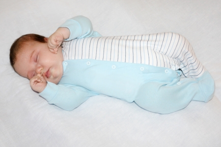 Little cute baby in blue jumper sleeps on white sheet on bed.の写真素材