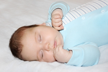 Little beautiful baby in blue jumper sleeps on white sheet on bed.の写真素材