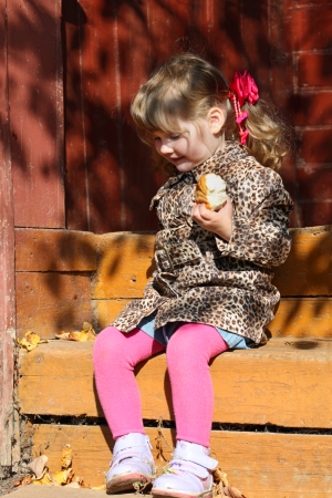 Pretty little girl with bun sits on wooden stairs at sunny day.の写真素材