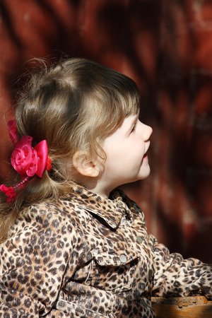 Pretty little girl with pink bows in overcoat looks up at sunny day.の写真素材