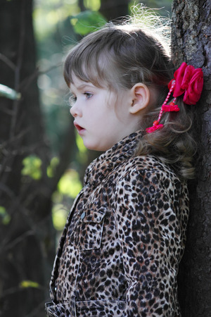 Pretty little girl with pink bows in overcoat looks away in forest.の写真素材