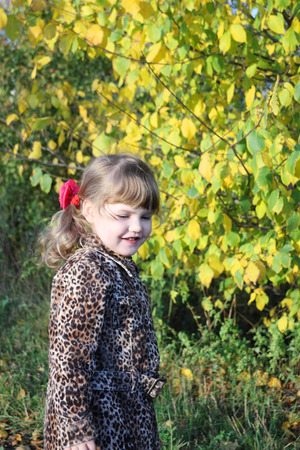 Happy little girl smiles next to yellow trees in park at sunny autumn day.の写真素材