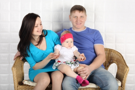 Young father, beautiful mother and cute baby sit on wicker sofa at home.の写真素材
