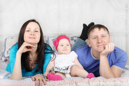 Young father, beautiful mother and cute baby lie on bed at home.の写真素材