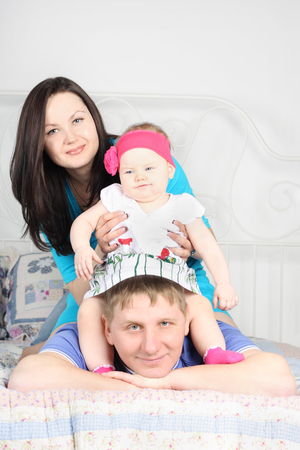 Beautiful mother and cute baby sit on father lying on bed at home.の写真素材