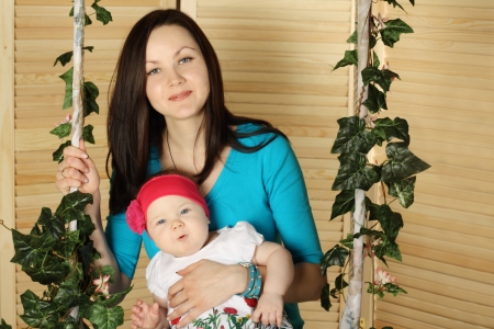 Happy mother with smiling baby sits on swing overgrown with green ivy.の写真素材