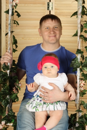 Happy father with cute baby sits on swing overgrown with green ivy.の写真素材