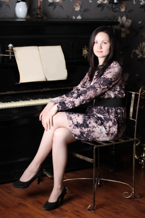 Beautiful young woman in dress sit at black old piano with music.の写真素材