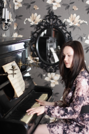 Beautiful young brunette woman in dress plays piano and sings. Focus on keys.の写真素材