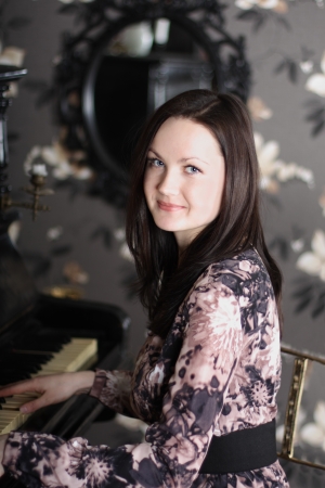 Beautiful young brunette woman in dress plays piano and looks at camera.の写真素材