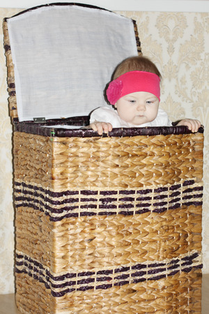 Little cute baby sits in big wicker basket and peeps out in room.の写真素材