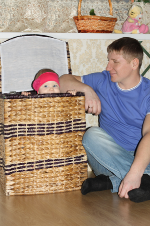 Little baby sits in big wicker and her happy father looks at she in room.の写真素材