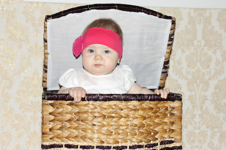 Little beautiful baby sits in big wicker basket and peeps out in room.の写真素材