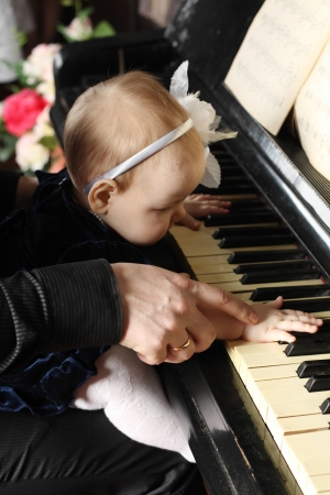 Cute baby sits at knees of her father and plays piano in room. Focus on hands.の写真素材