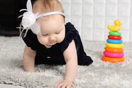 Little baby in dress creeps on grey soft carpet with colorful toy pyramid.の写真素材