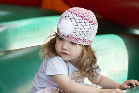 Little beautiful girl in openwork hat on green inflatable trampoline.の写真素材
