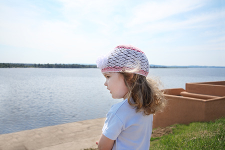 Little girl looks at blue waters of river at sunny summer day.の写真素材