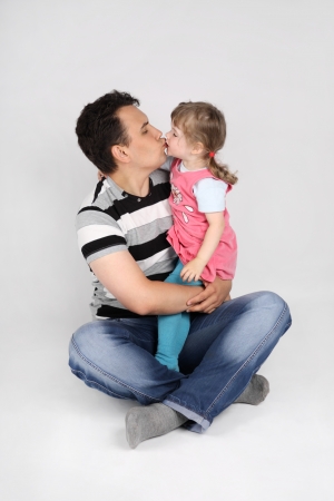 Little cute daughter kisses her father sitting on floor on grey background.の写真素材