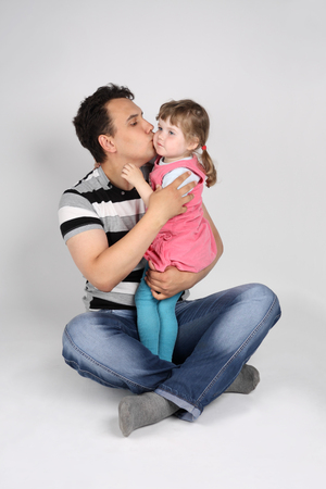 Father holds and kisses his little cute daughter on floor on grey background.の写真素材
